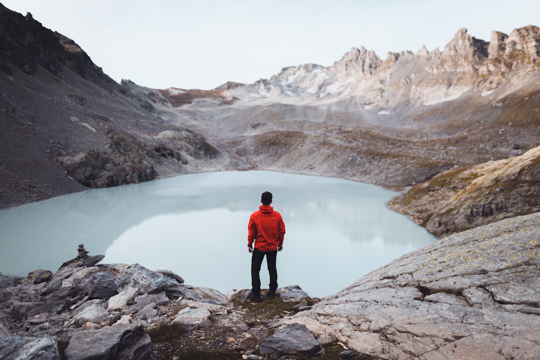 man in red jacket standing on rocky mountain near lake during daytime