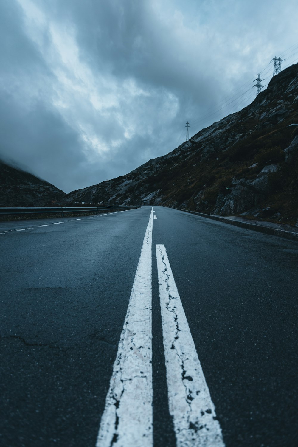 gray asphalt road between mountains under white clouds and blue sky during daytime