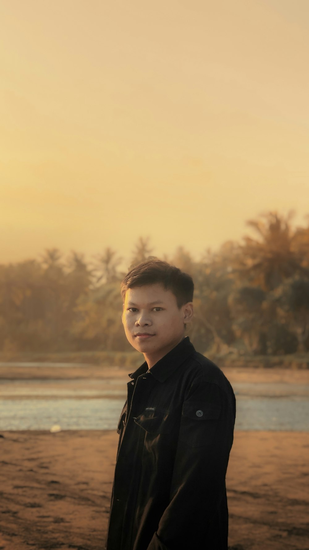 man in black jacket standing near body of water during sunset