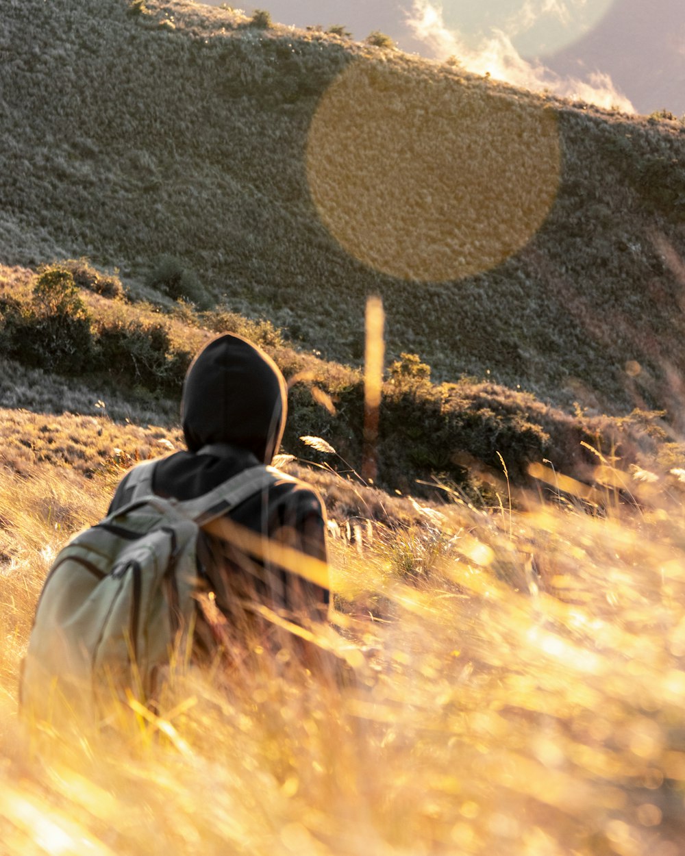 man in black hoodie and black knit cap sitting on brown grass field during daytime