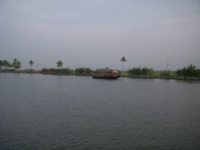 A serene backwater scene in Kerala with a traditional houseboat floating gently on calm waters at sunset.