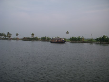 A serene view of a traditional houseboat gliding through the backwaters of Kerala surrounded by lush greenery.