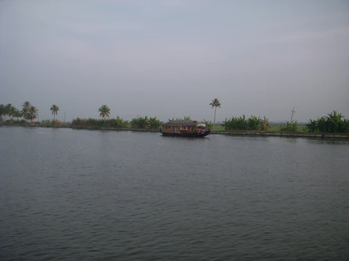 A serene backwater scene in Kerala with a traditional houseboat floating gently on calm waters at sunset.