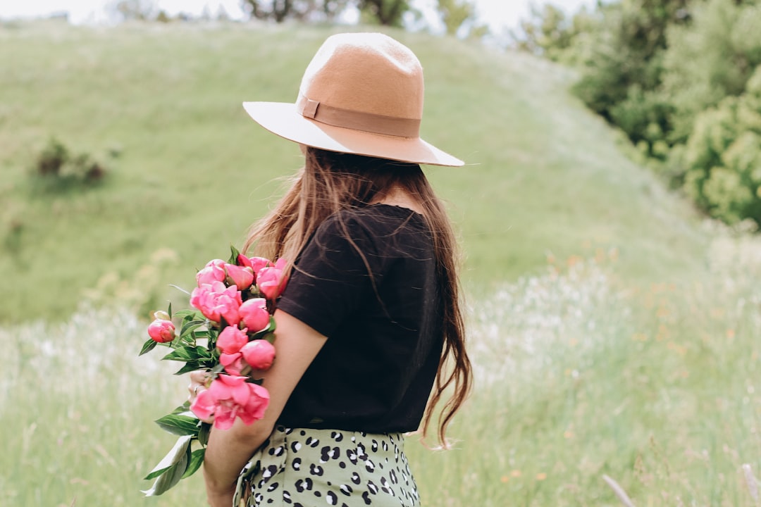 woman in black and white polka dot dress with brown hat holding red flowers