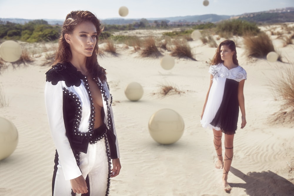 woman in black and white long sleeve shirt and white pants standing on sand during daytime