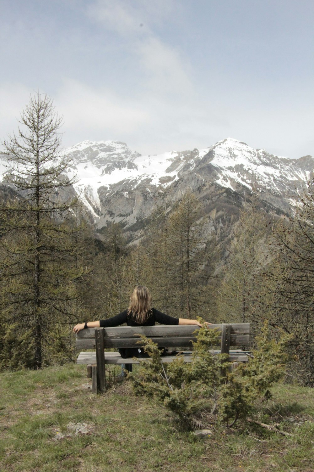 Mujer sentada en un banco de madera marrón cerca de una montaña cubierta de nieve durante el día
