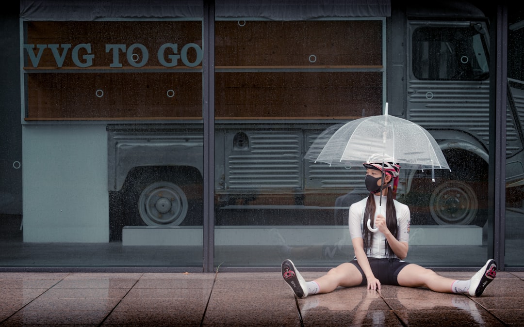 woman in white tank top sitting on sidewalk holding umbrella