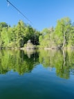 Angler casting a line into a calm lake surrounded by pine trees.