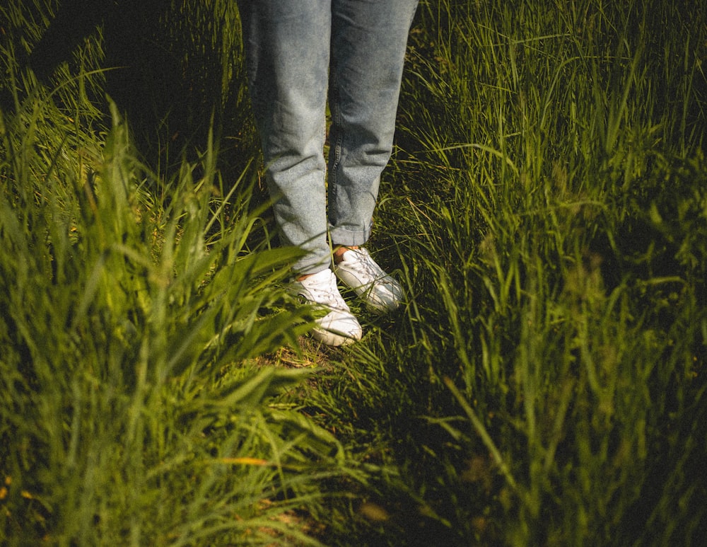 緑の草原に立つ青いデニムジーンズと白いスニーカーを履いた人
