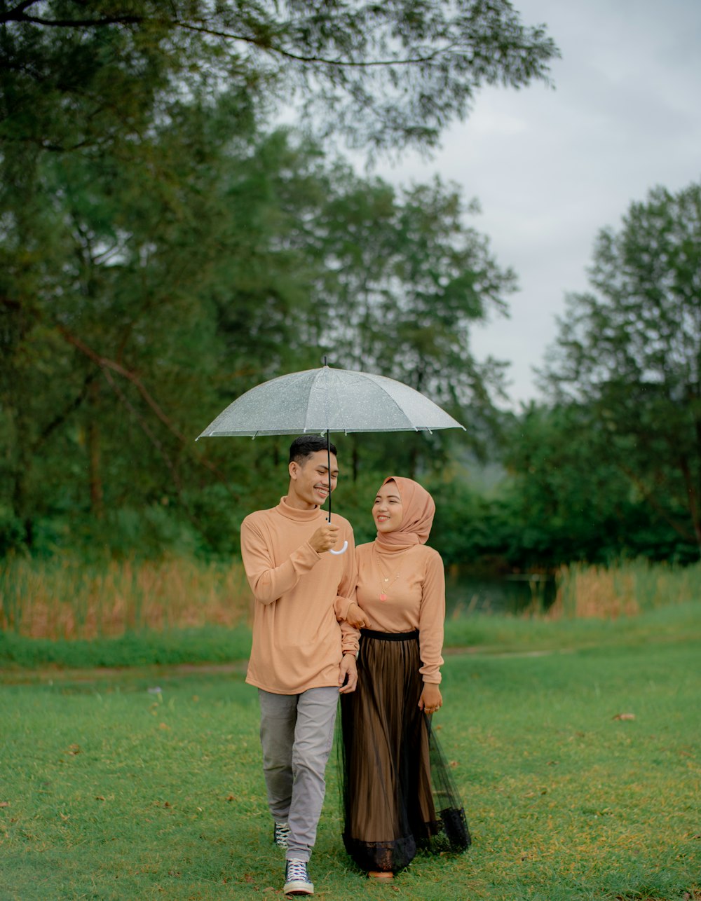 Frau im braunen Mantel mit Regenschirm, die tagsüber auf grünem Grasfeld geht