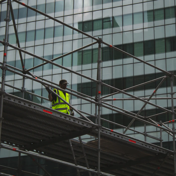 Scaffolder in hi-vis working on a platform against a glass office building