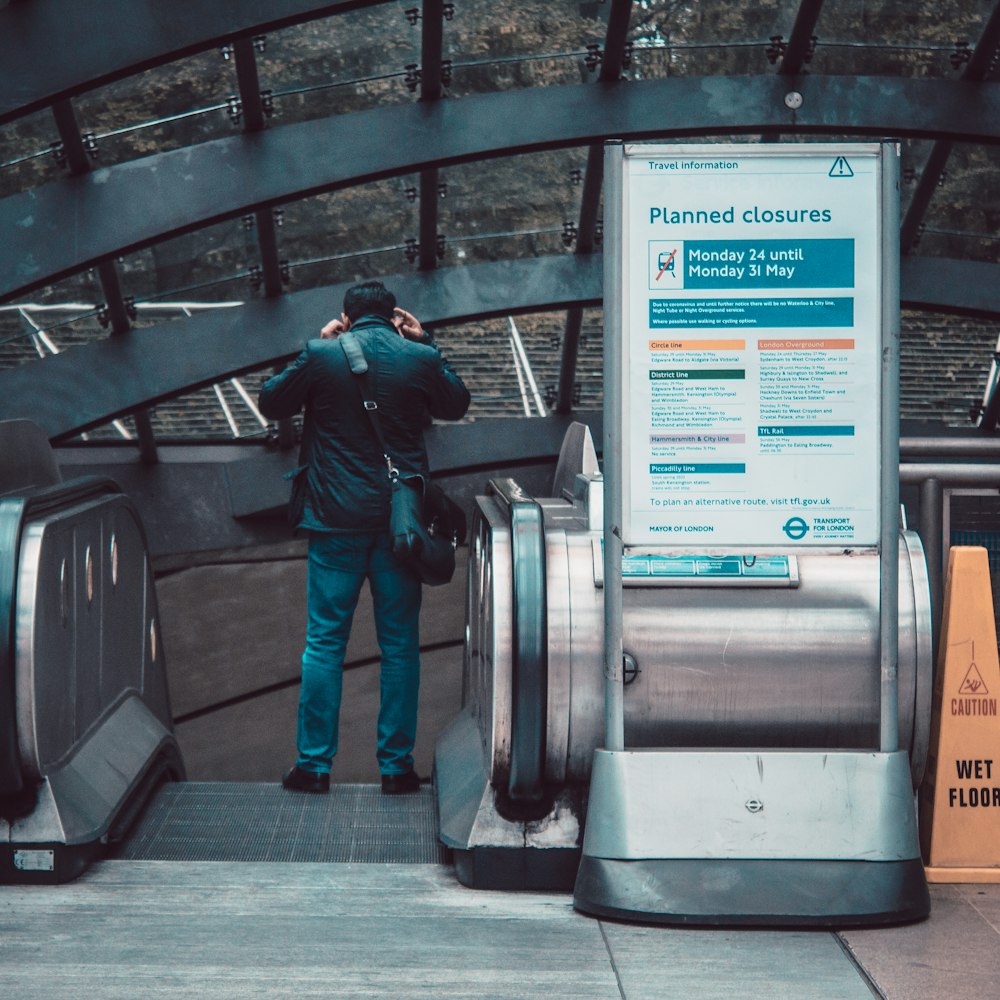 man in green jacket and blue denim jeans standing on escalator