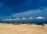 Sandy beach with clear blue water and sun loungers near the shore.