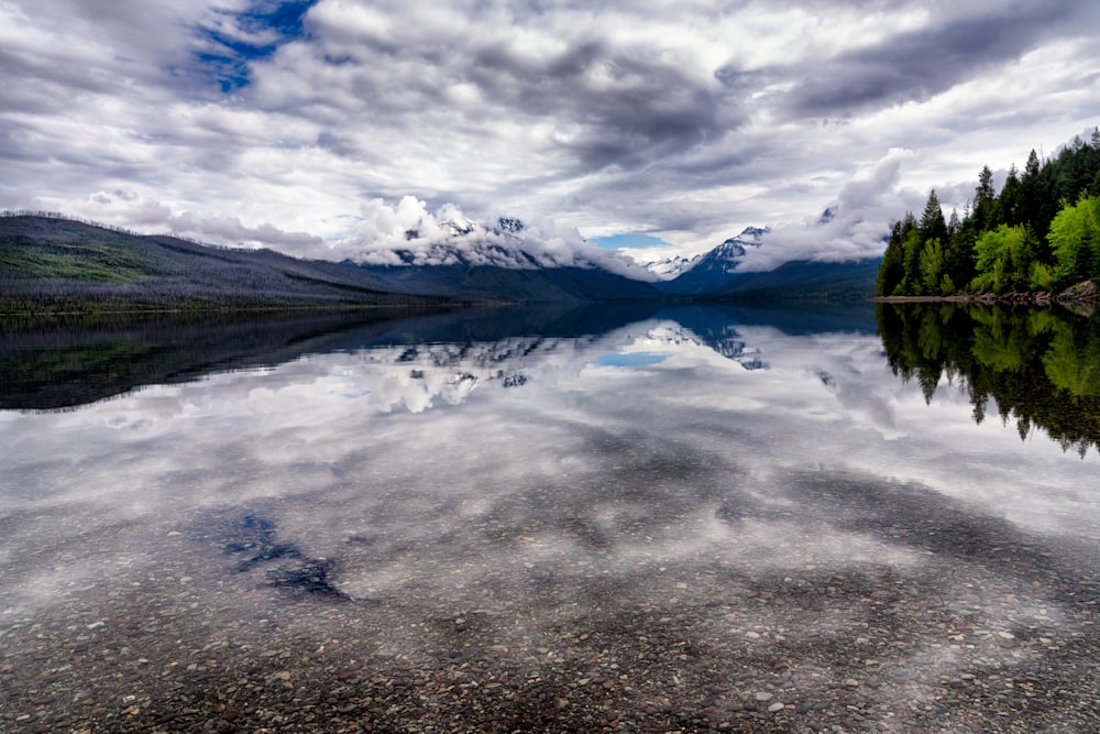 body of water near mountain under cloudy sky during daytime