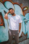 man in white crew neck t-shirt and black pants standing beside wall with graffiti
