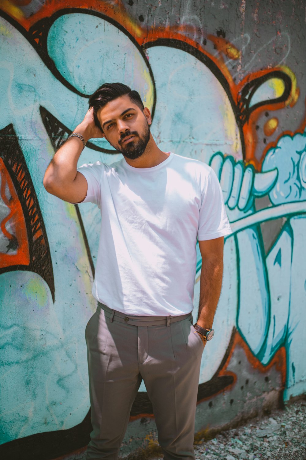 man in white crew neck t-shirt and black pants standing beside wall with graffiti