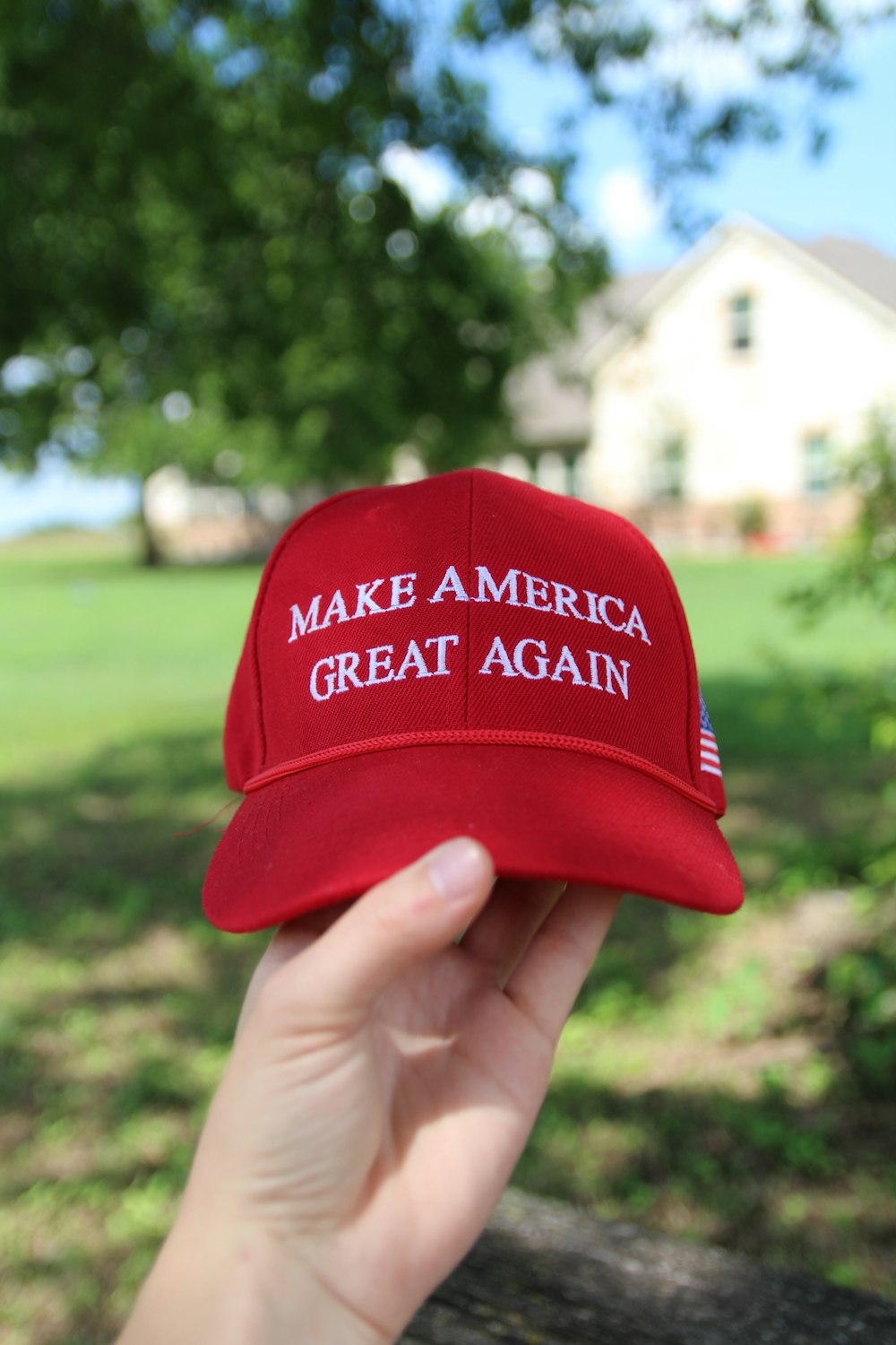 a person holding up a red hat that says make america great again
