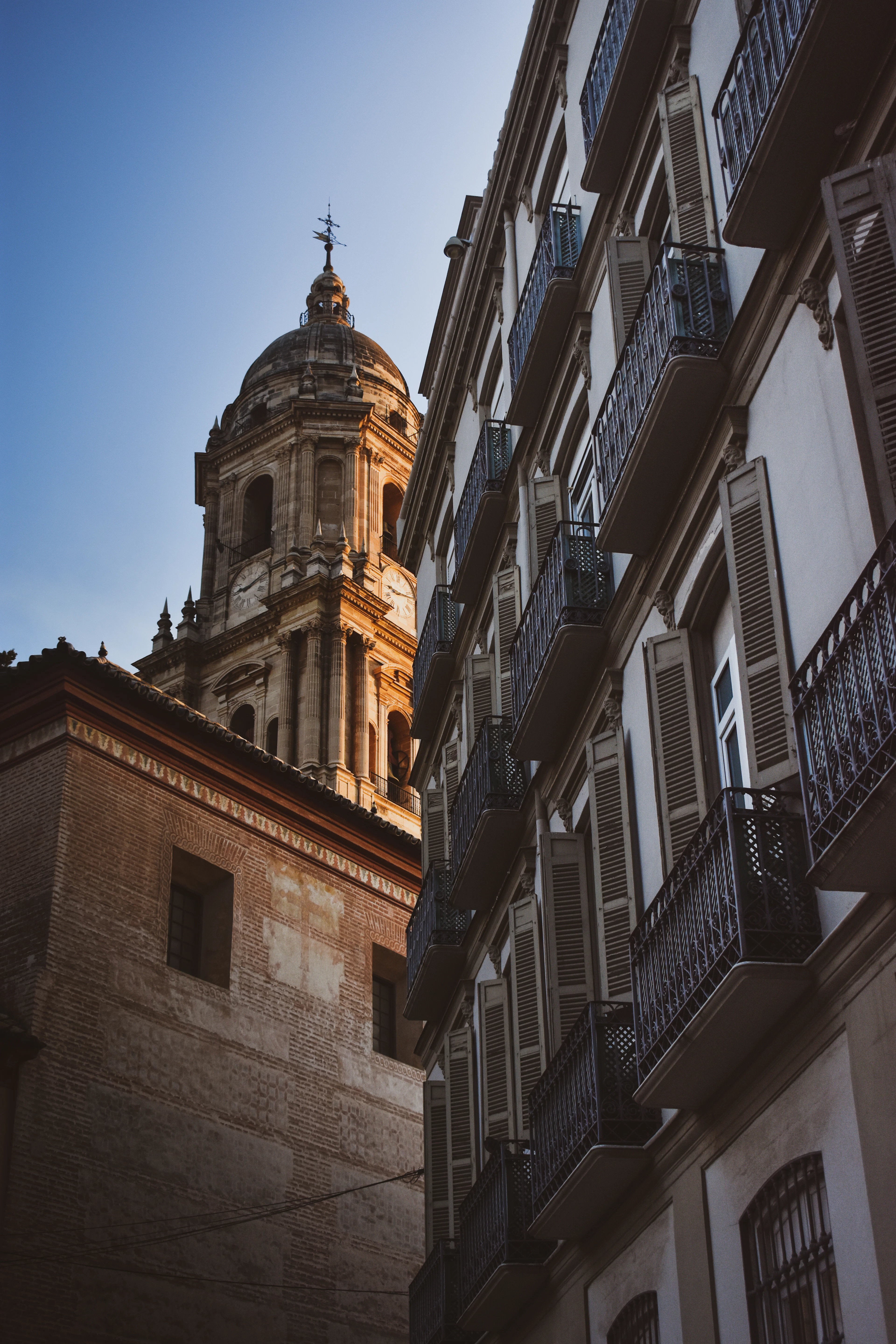 Málaga Cathedral's ornate bell tower glows in late sunlight above a narrow street.
