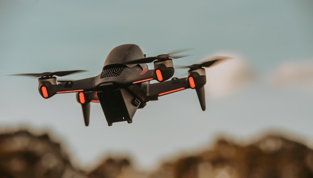 gray and orange drone flying in mid air during daytime