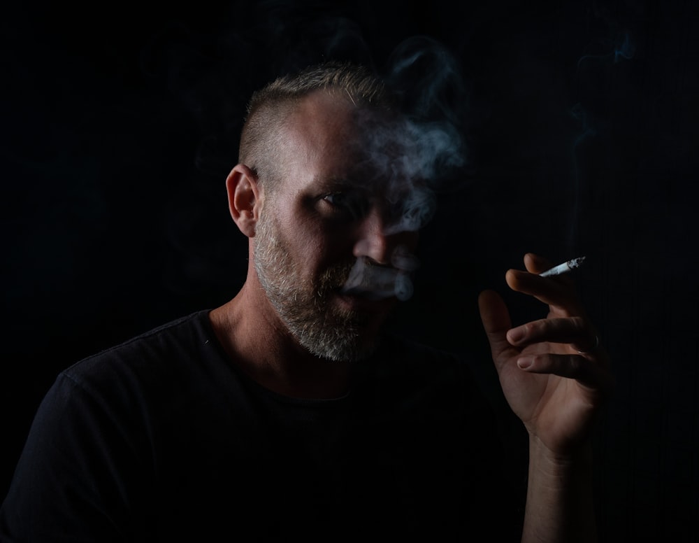 homme en chemise à col rond noir fumant une cigarette