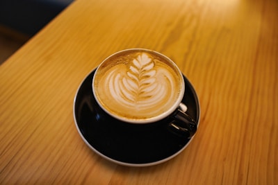 Barista carefully pouring latte art in a sleek black cup on a wooden table.
