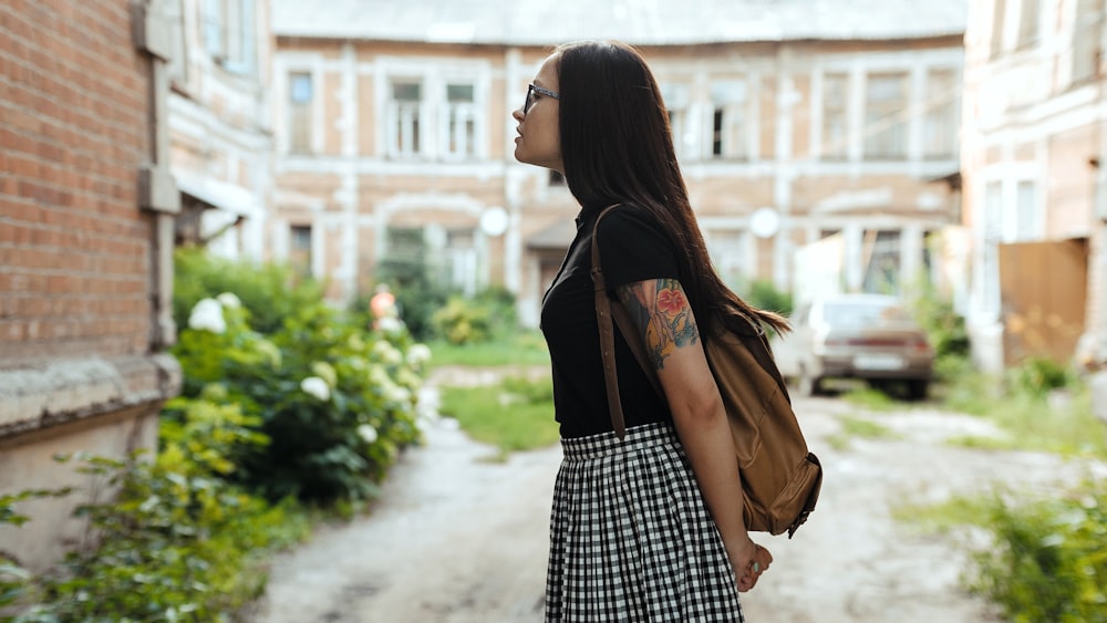 woman in black and white checked skirt and brown leather jacket standing on sidewalk during daytime