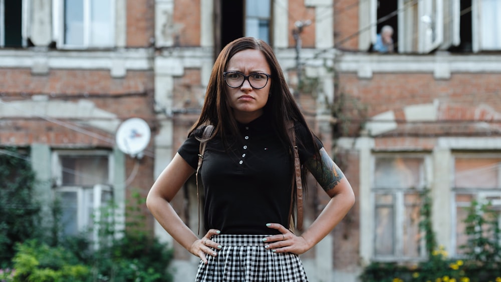 woman in black scoop neck shirt and black and white checkered skirt standing near brown concrete