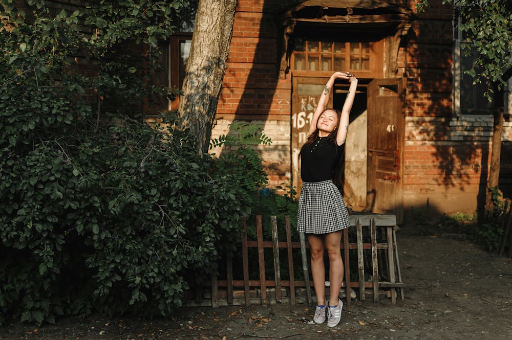 woman in black sleeveless dress standing near brown wooden house during daytime