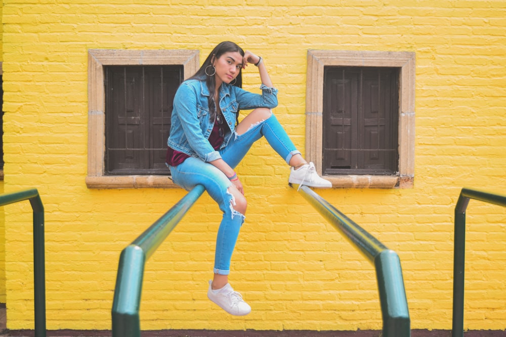 woman in blue denim jacket and blue denim jeans sitting on green metal railings