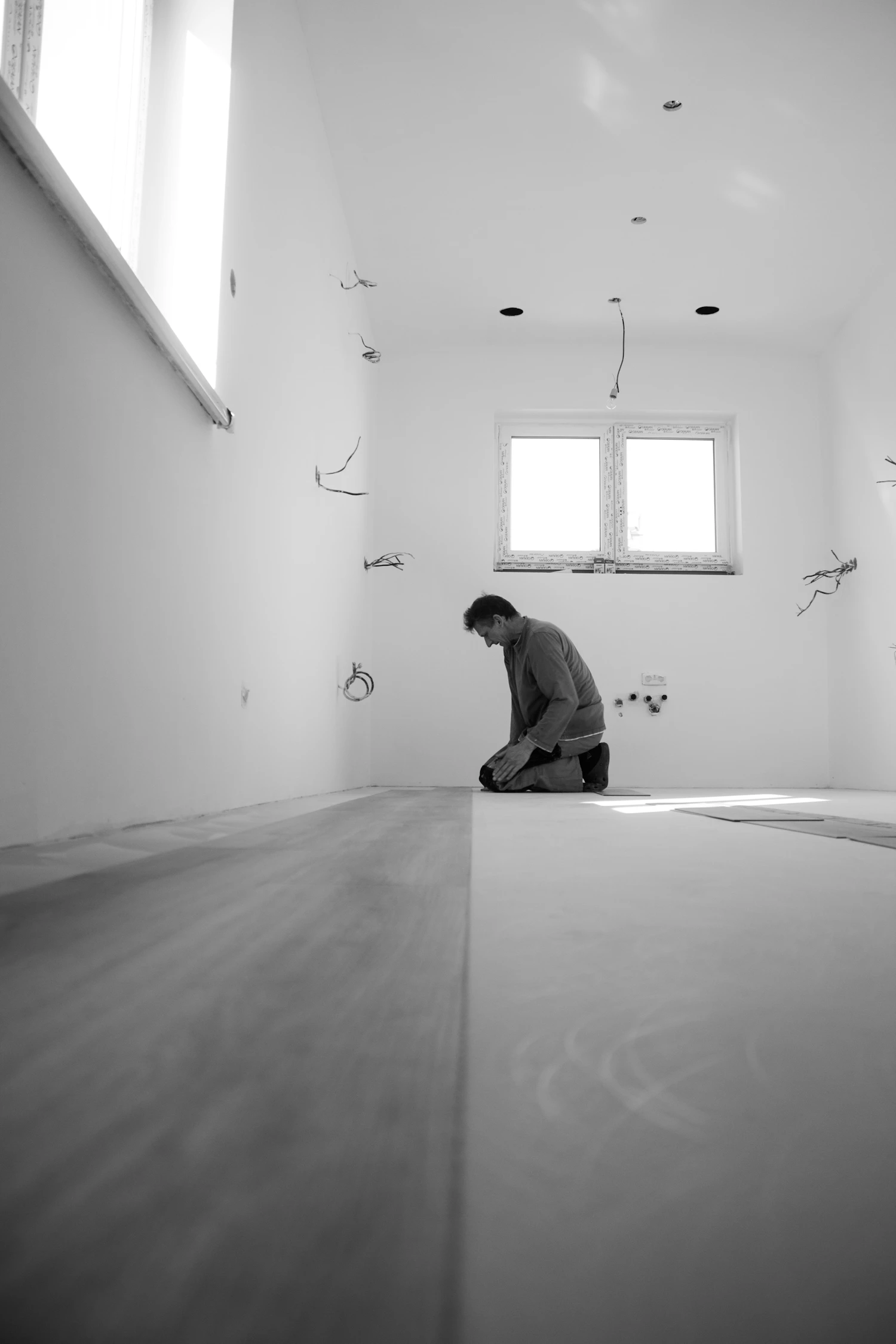 Black-and-white photograph of an installer kneeling beside flooring planks