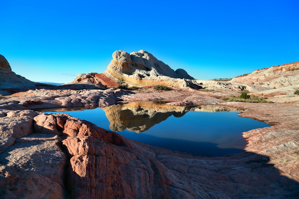 brown rocky mountain beside blue lake under blue sky during daytime