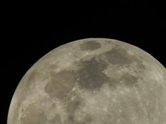 A close-up view of the moon, showing detailed surface features and craters on its surface, set against a black night sky.