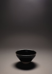 Pearl white ceramic vessel resting on natural wood with soft light.