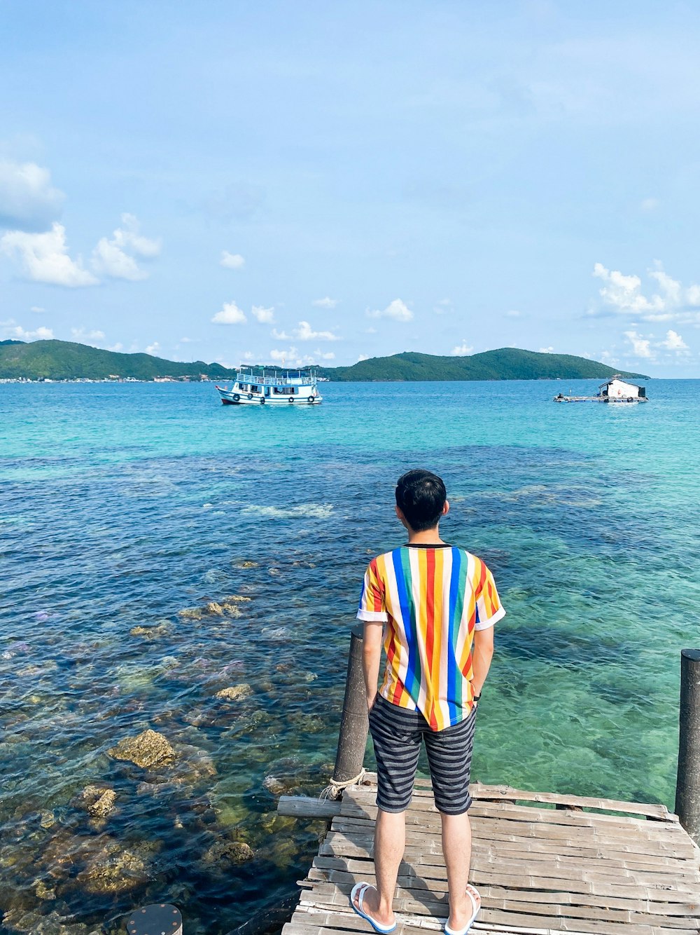 man in orange white and black stripe shirt standing on dock during daytime