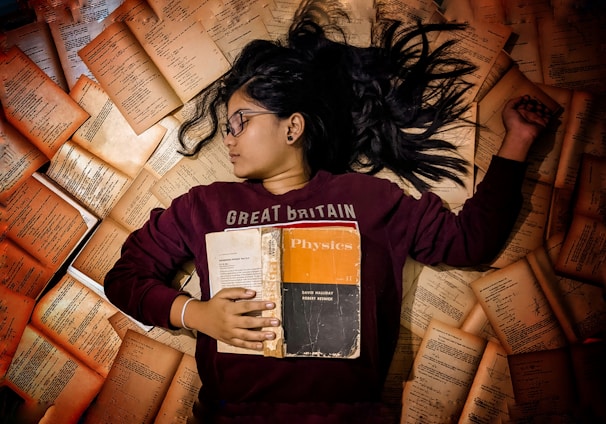 woman in red long sleeve shirt holding orange and white book