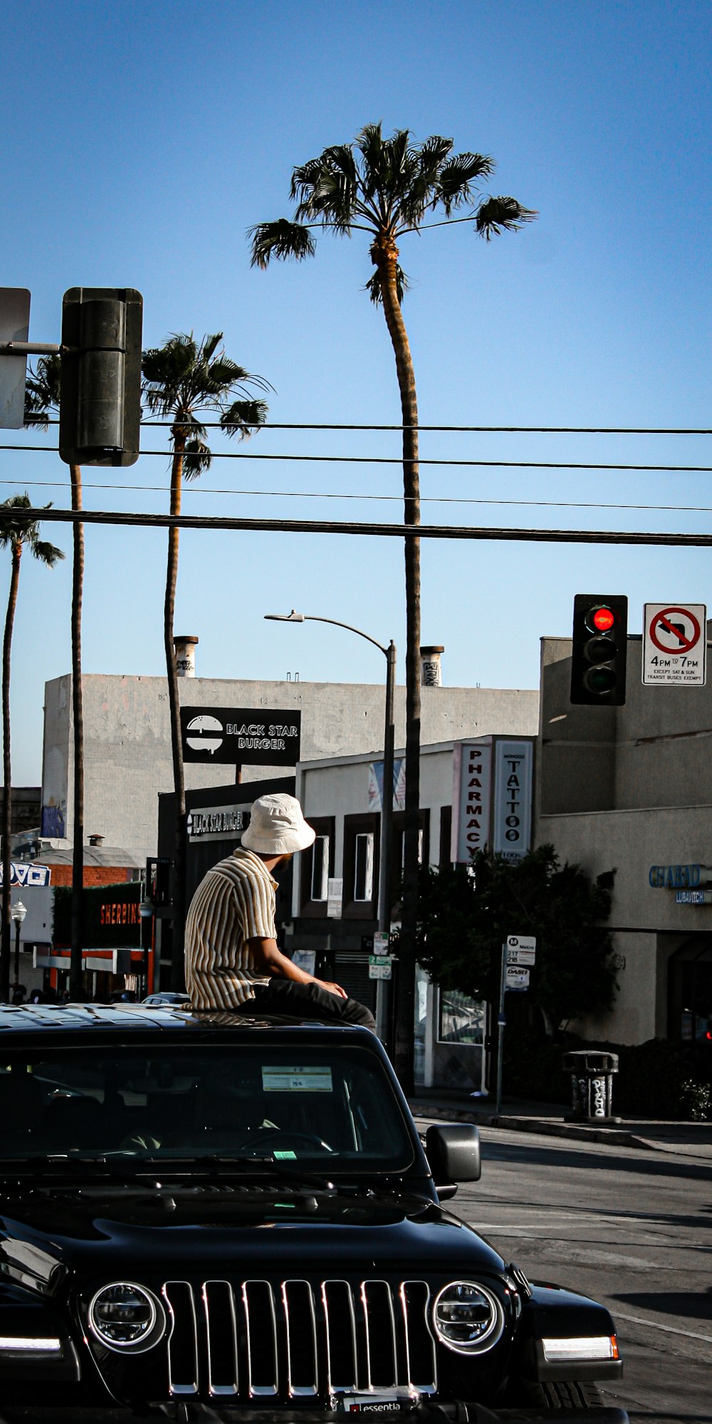 Mann in weiß-schwarz gestreiftem Hemd und braunem Hut sitzt tagsüber auf dem Bürgersteig