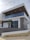 A modern, two-story building with a minimalist design features a flat roof and large glass windows. The upper level includes a balcony enclosed with transparent glass railings. The façade incorporates a combination of white and gray tones with a touch of natural wood and stone elements.