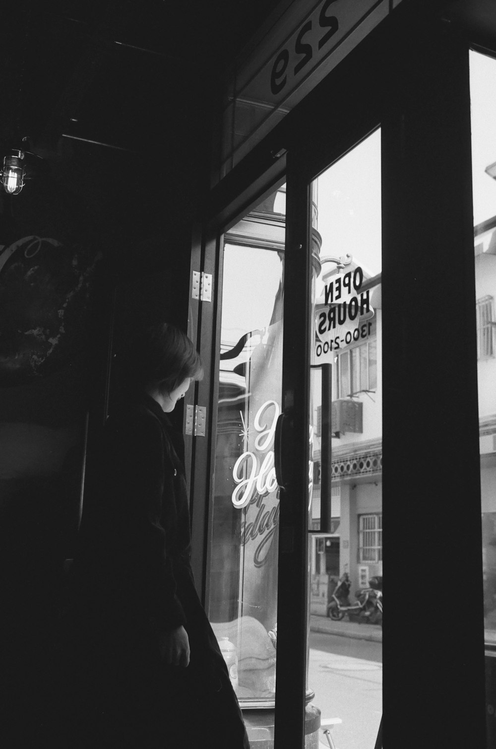 grayscale photo of man in jacket standing in front of store