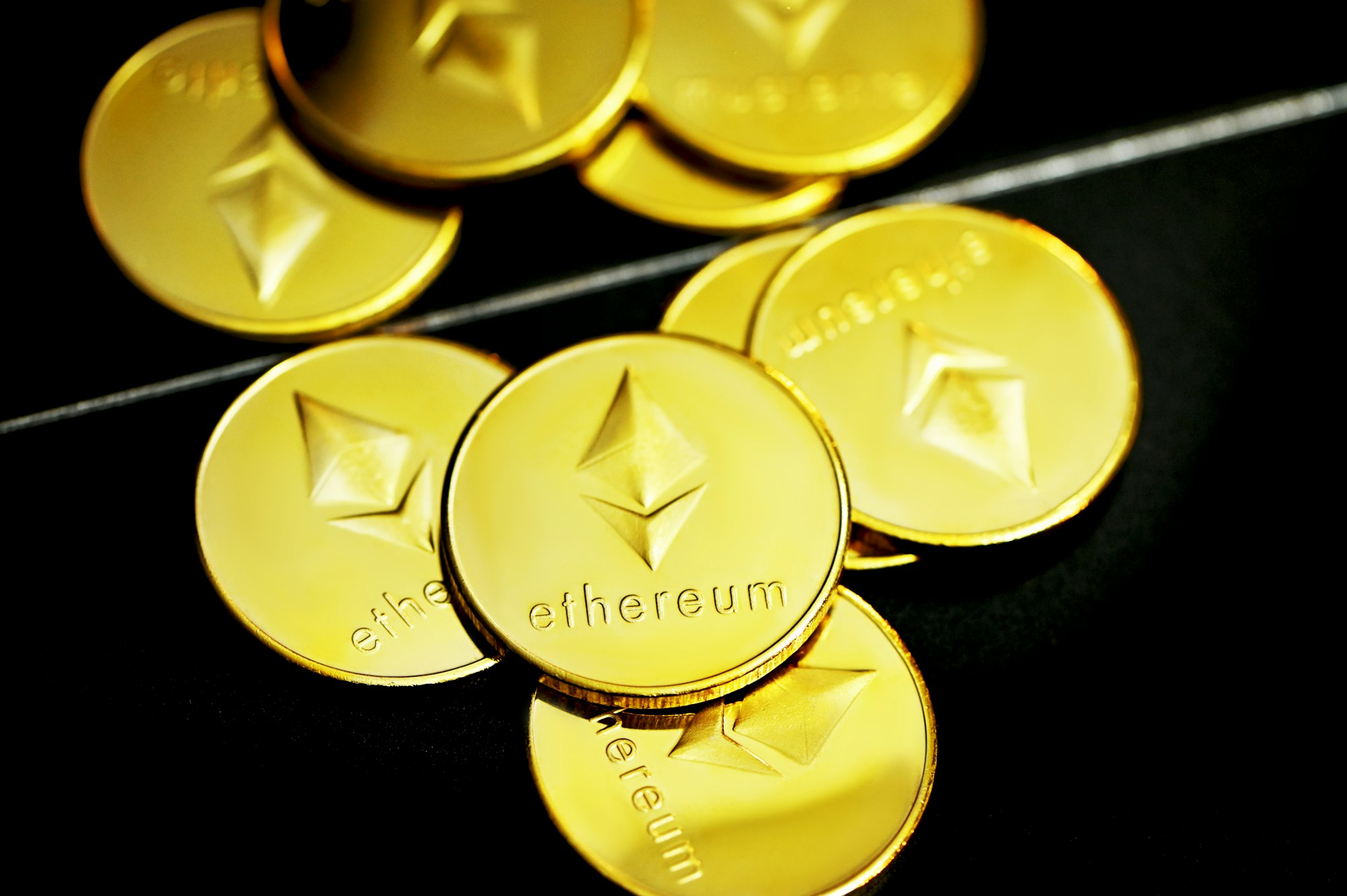 Ethereum coins on a black surface in front of a mirror