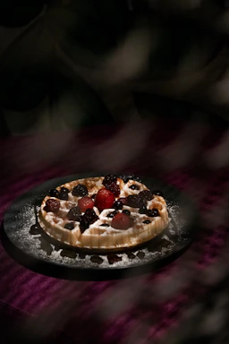 A vibrant waffle topped with fresh berries, cream, and a drizzle of chocolate sauce on a rustic wooden table.