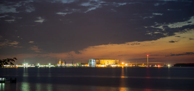 An industrial terminal at dusk, with muted reflections on water and minimal ambient light.