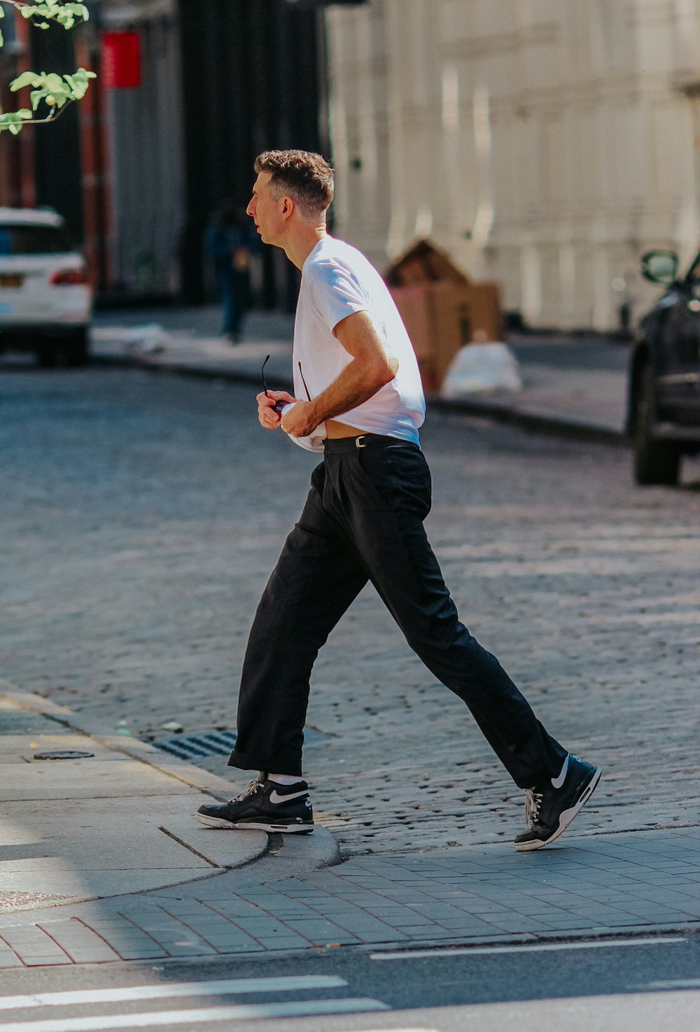 man in white t-shirt and black pants walking on sidewalk during daytime