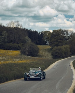 black car on road between green grass field during daytime