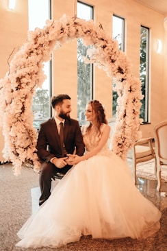 man in black suit and woman in white wedding dress sitting on chair