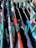 Various colorful clothes are hung to dry on a drying rack, secured with teal clothespins. The clothes are in shades of red, blue, black, white, and gray.