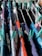 Various colorful clothes are hung to dry on a drying rack, secured with teal clothespins. The clothes are in shades of red, blue, black, white, and gray.