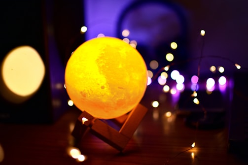 A close-up photo of a customized 3D printed moon lamp glowing softly on a decorated table.