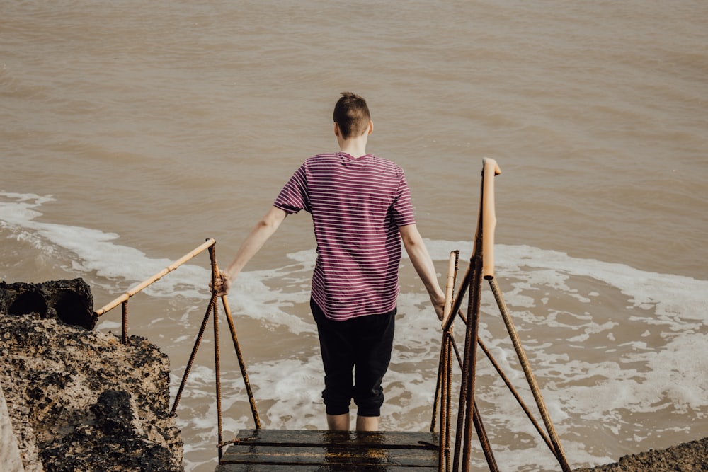 man in red and white stripe shirt and black pants standing on brown wooden dock during