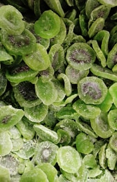 Thinly sliced pieces of dried kiwi with a sugary coating are layered in abundance. The vibrant green slices display their unique texture and seeds, adding visual interest and indicating their fruit origin.