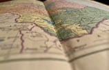 A close-up view of a colorful, detailed map, slightly out of focus in the foreground, with visible borders, names of countries, and geographical features.